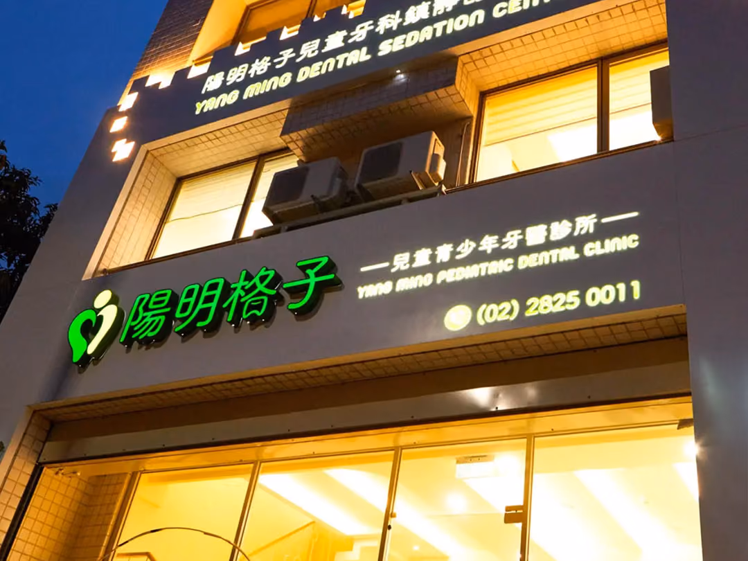 暮色仰角拍攝,下段大型立體字發綠光,上段與右側文字發暖白光,一樓玻璃門面與室內透出暖黃光,天空深藍