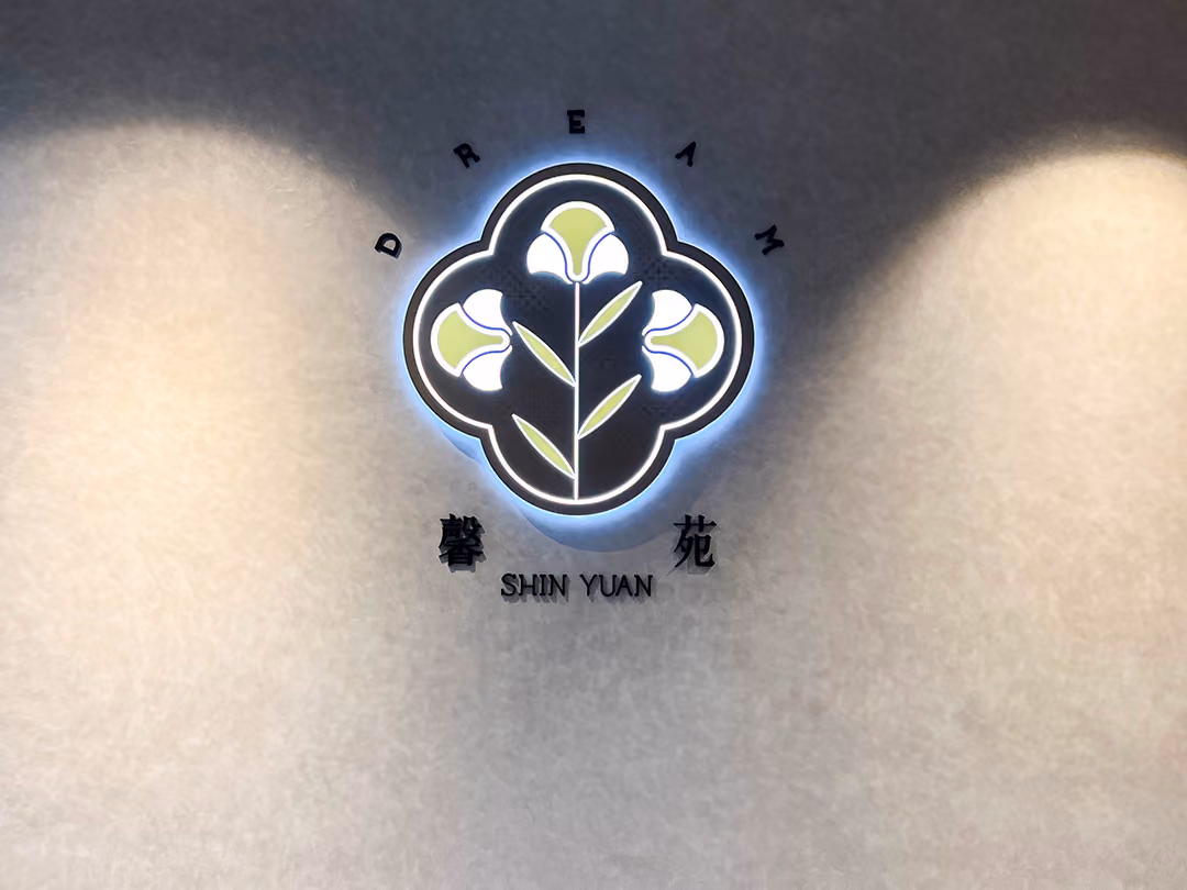 正面視角,白紋理牆中央的深色花形標誌背光點亮成冷白光圈,兩側各有一道自上而下的光暈